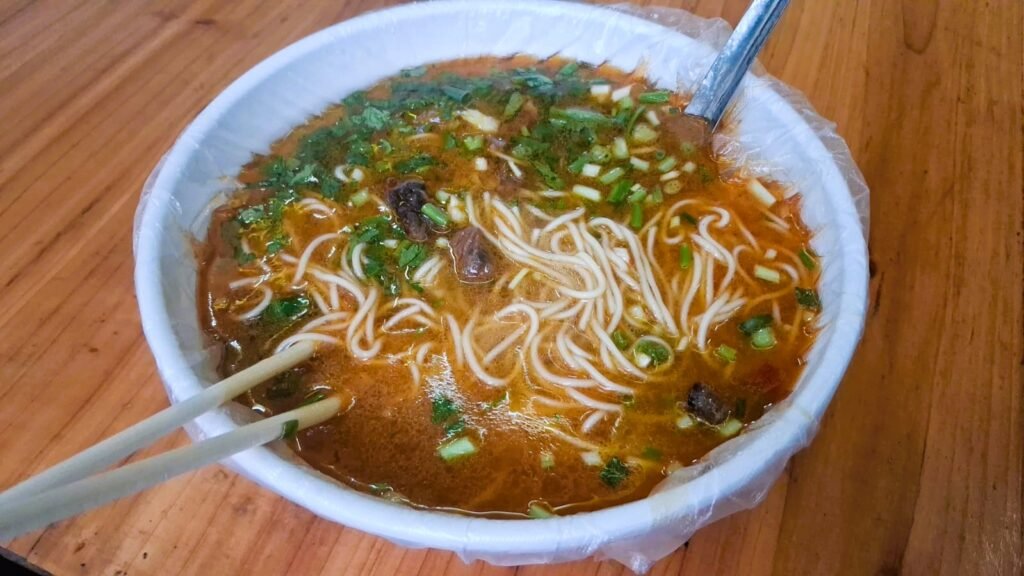 A bowl of beef noodle soup with rich orange broth and toppings from a night market in Hainan China