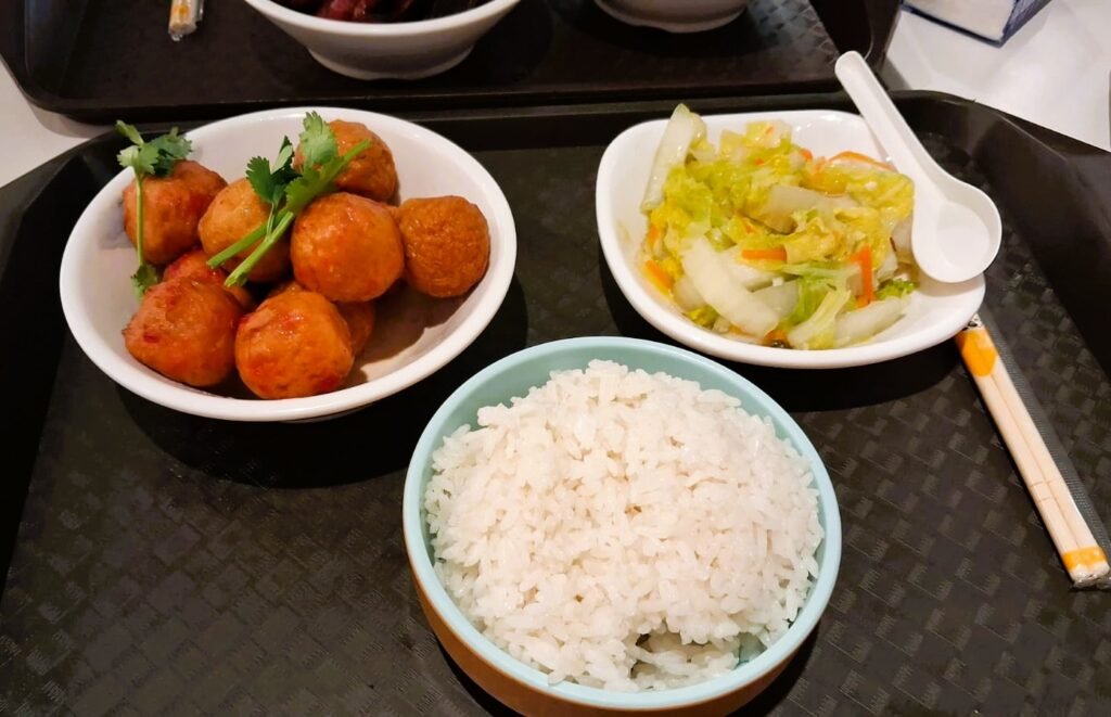 A tray of fish meatballs in sauce, a bowl of steamed rice, and a napa cabbage side dish at a food court in Hainan China